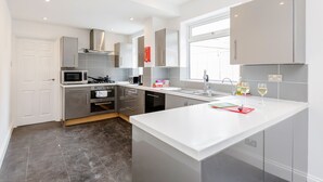A modern kitchen with grey cabinets, a white countertop, and a window providing natural light. - Westland House Guest house (Watford)