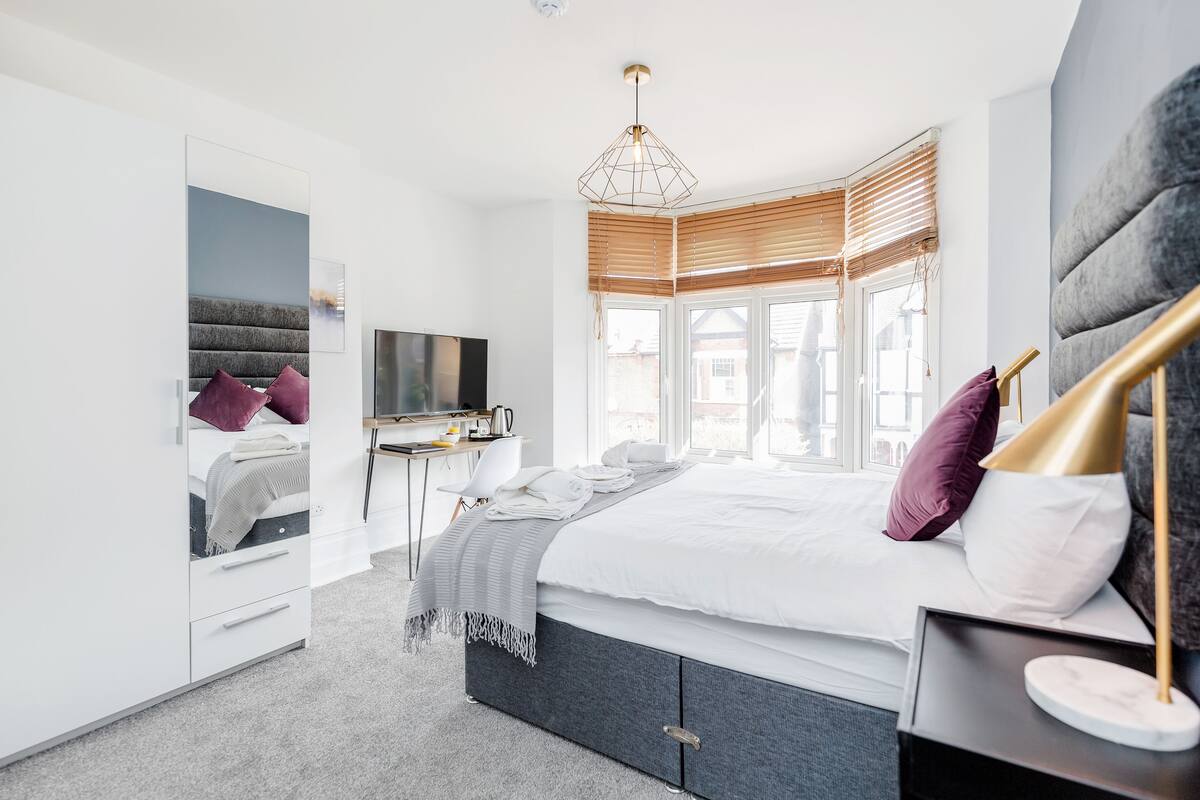 A modern bedroom with a large bed, a desk, and a TV.