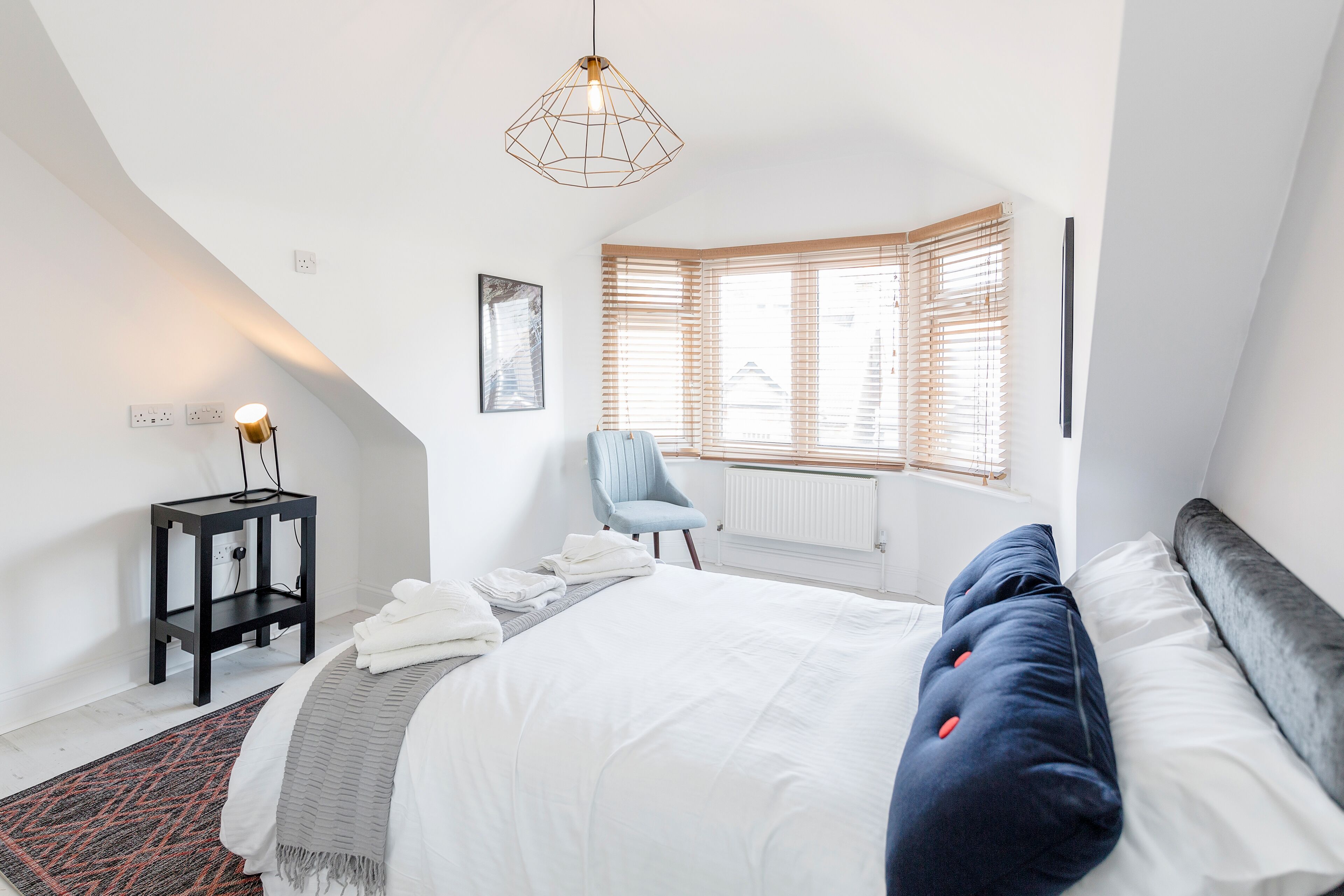 A bedroom with a bed, a chair, a desk, and a window with blinds.