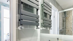 A modern bathroom with a large mirror, a white sink, and a towel rack. - Westland House Guest house (Watford)