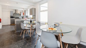 A modern kitchen with white cabinets, a microwave, and a dining area with a glass table and chairs. - Westland House Guest house (Watford)