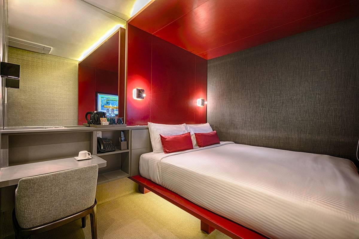 A hotel room with a bed, a desk, a chair, a TV, and a coffee machine.