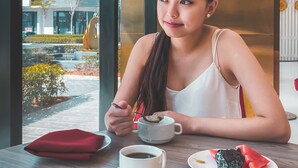 A person sitting at a table with a cup of coffee, a plate with food, and a window view of a building and outdoor area. - The Upper House Hotel (Simpang Ampat)