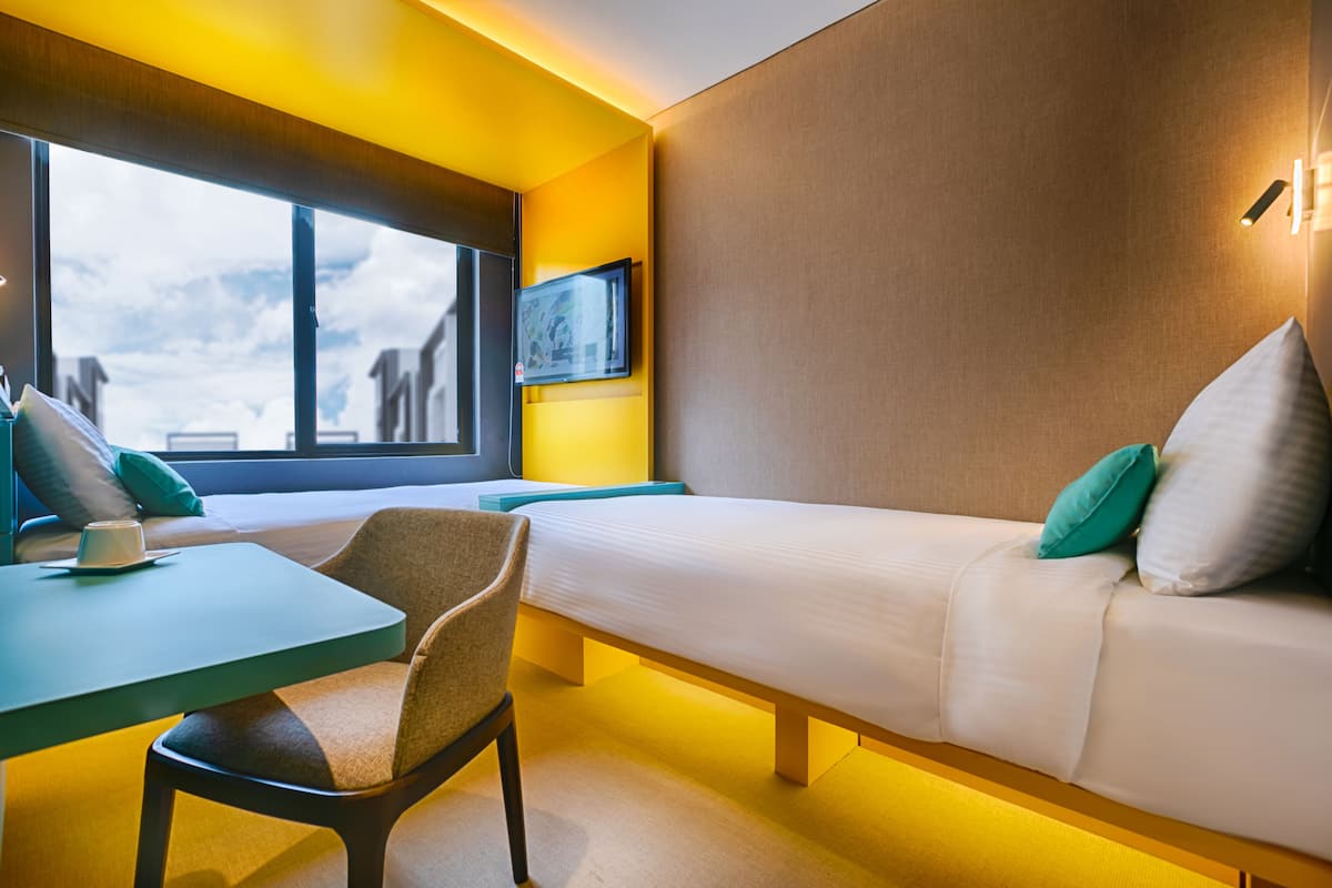 A modern room with a bed, a table, and a chair. There is a window with a view of buildings.