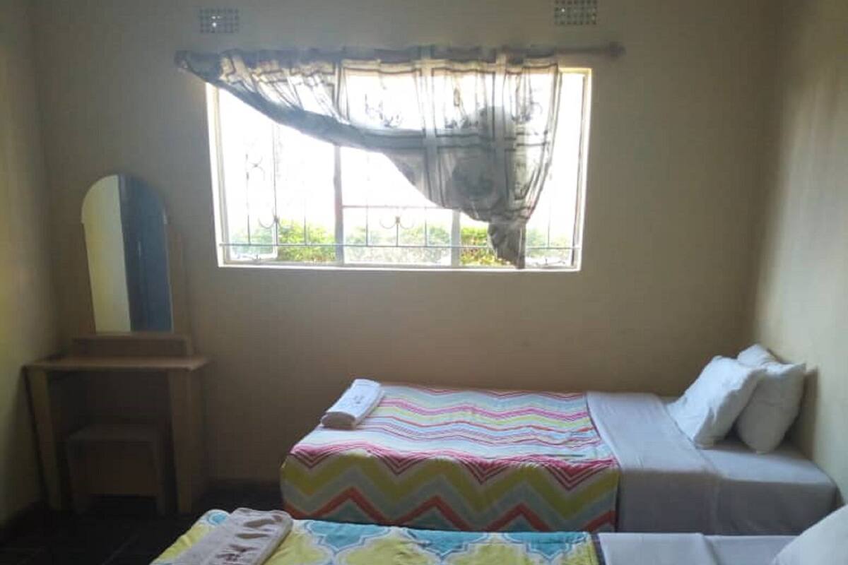 A room with two beds, a small table, and a window with a view of greenery.