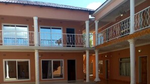 A spacious courtyard with a tiled floor, a two-story building with balconies, and large windows. - Kamuboola Lodge (Choma)