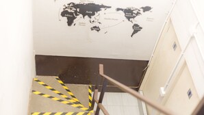 A stairway with yellow and black caution stripes leading to a room with a world map on the wall. - Lemon Siam Hostel Free Breakfast (Bangkok)