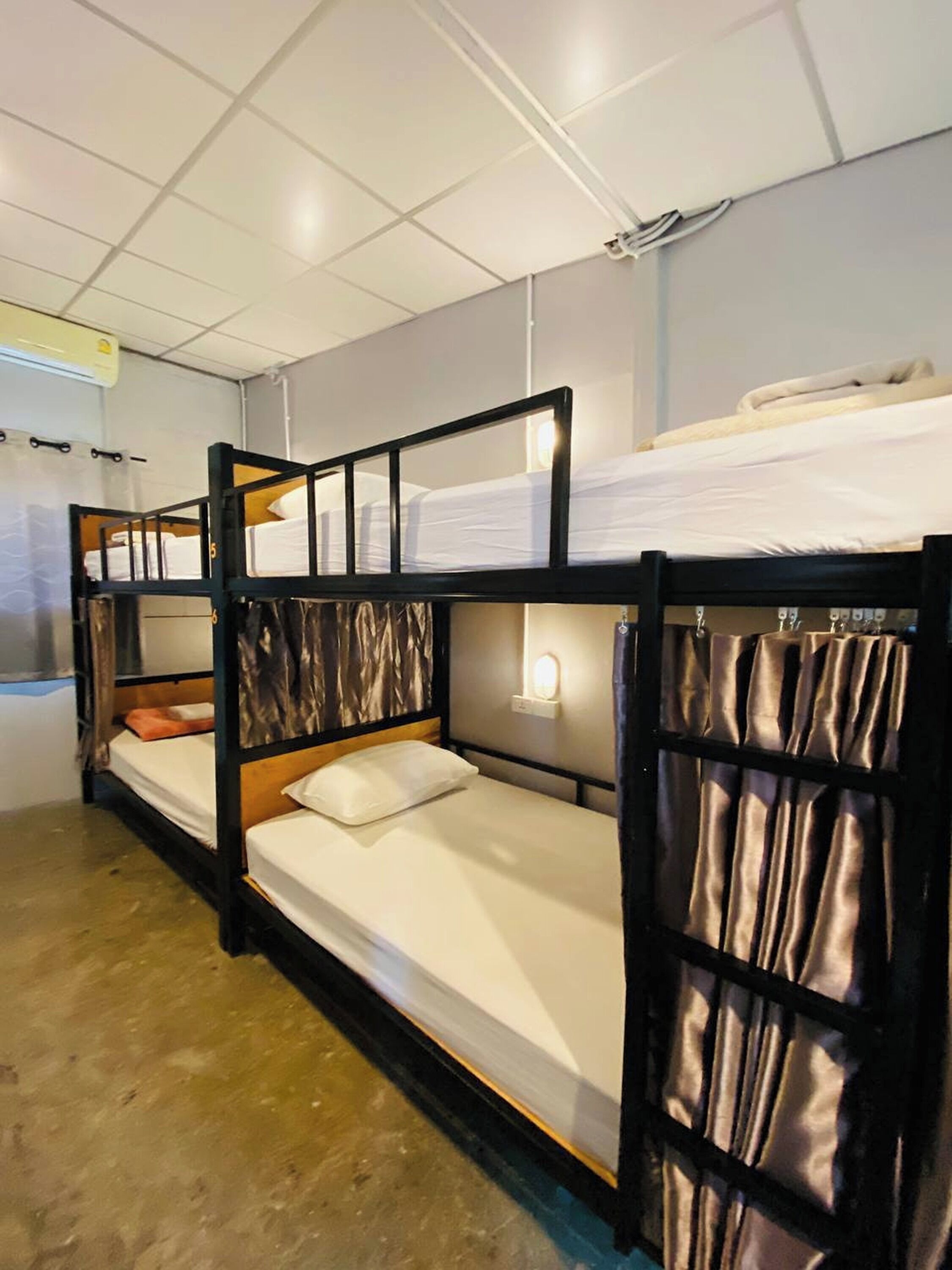 A bunk bed room with a white ceiling, a wall-mounted light, and a window with curtains.