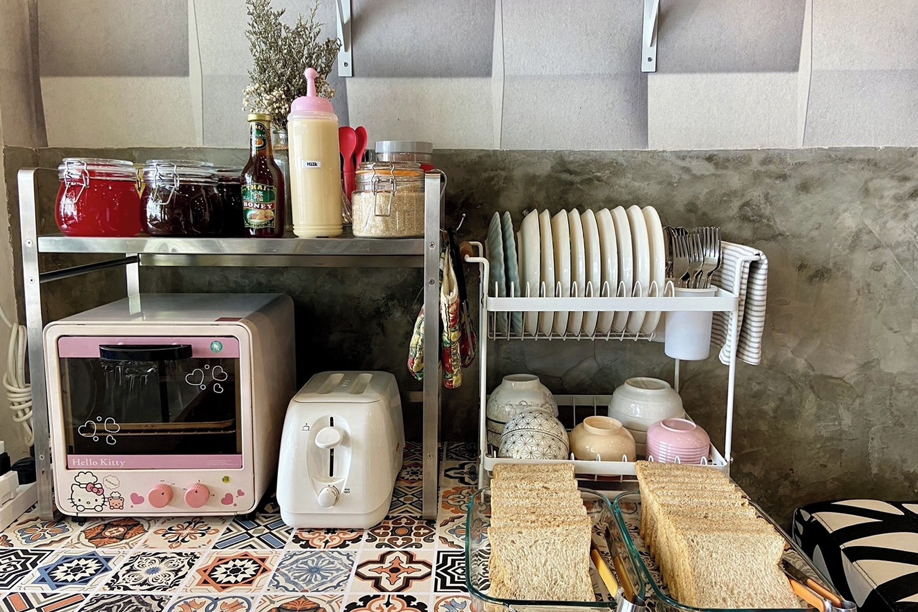 A kitchen with a toaster, a small oven, a bread rack, and various kitchen utensils.