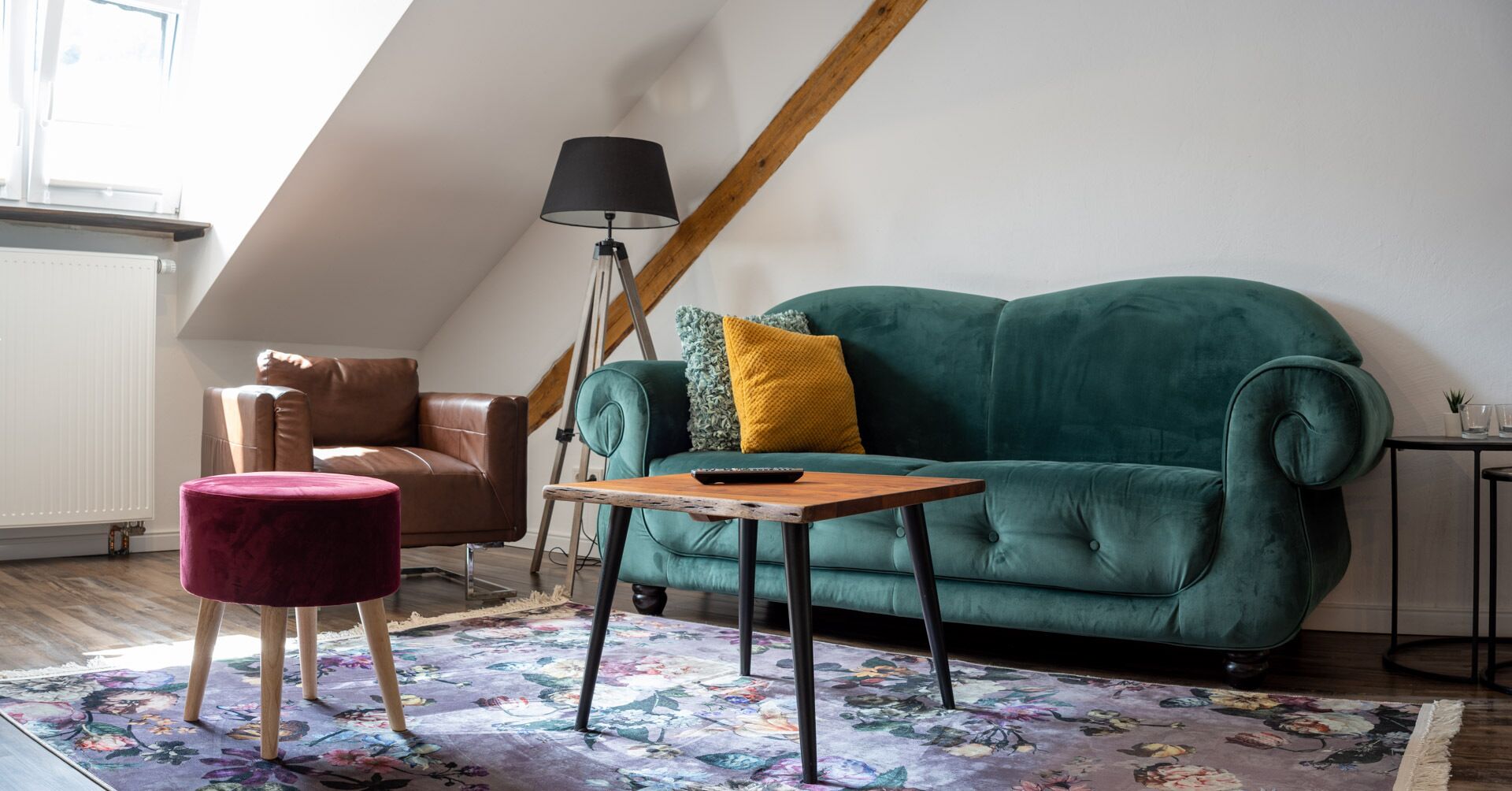 Une pièce chaleureuse, aménagée dans un style loft, avec un canapé en velours vert, un fauteuil en cuir marron, un petit pouf rond et une table basse en bois.