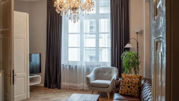 A living room with a large window, a chandelier, a television, a sofa, and a plant. - Das Haus Am Markt (Traben-Trarbach)