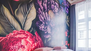 A bedroom with a large floral mural, a bed with pink bedding, and a small bedside table with a lamp. - Das Haus Am Markt (Traben-Trarbach)