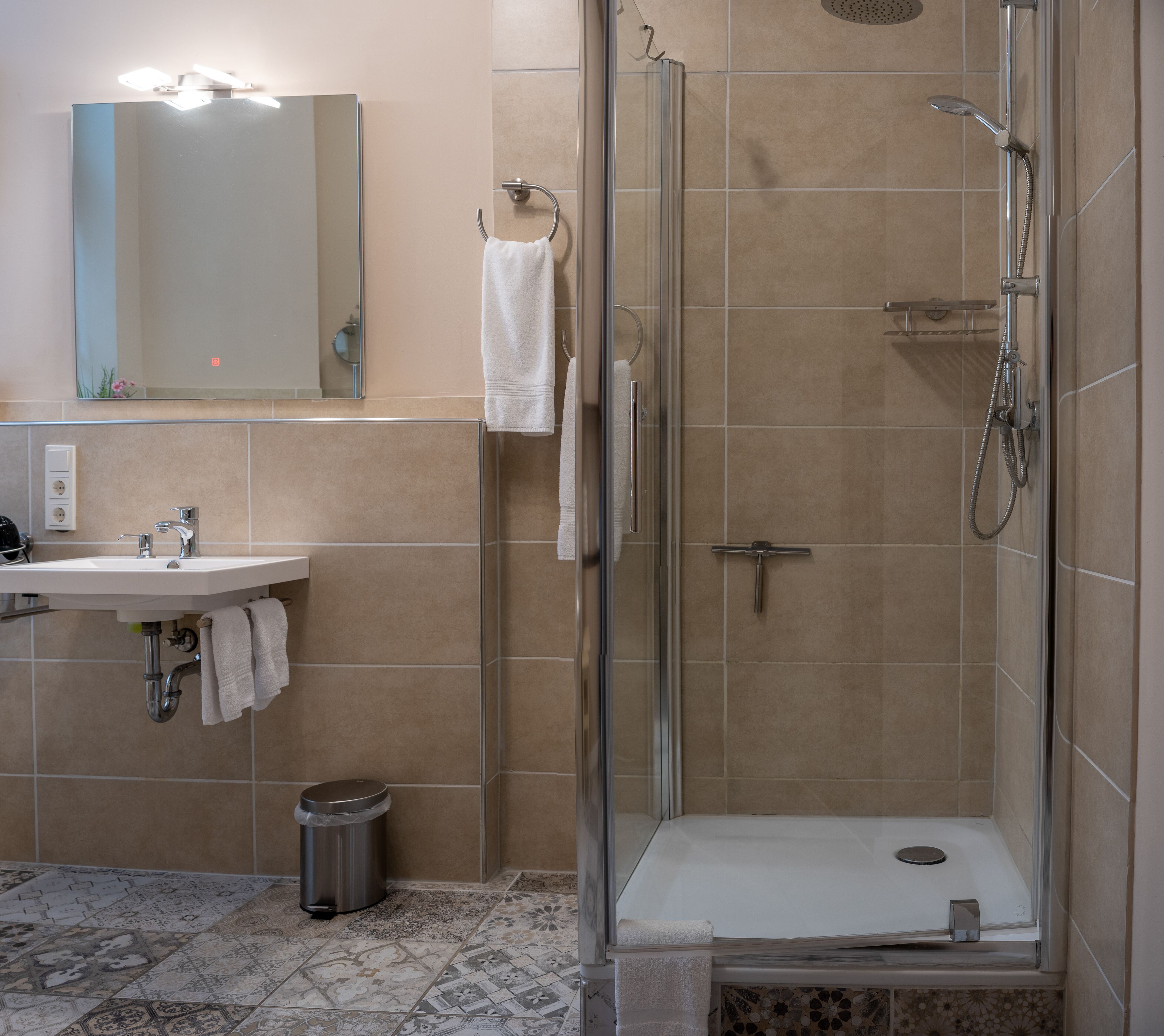 A bathroom with a sink, mirror, towel rack, shower, and tiled floor.
