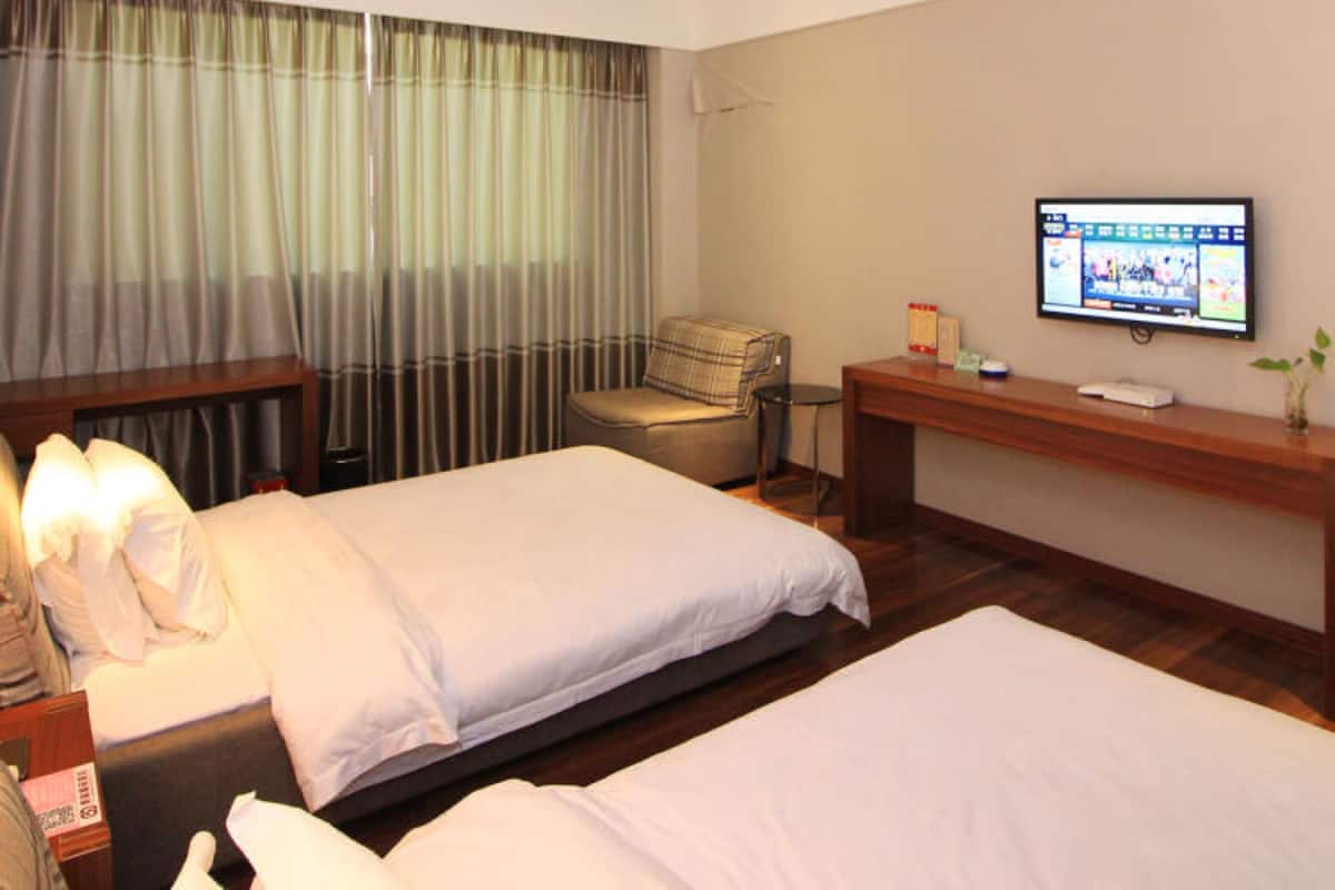 Une chambre d’hôtel avec deux lits, un bureau, une télévision et une fenêtre avec des rideaux.