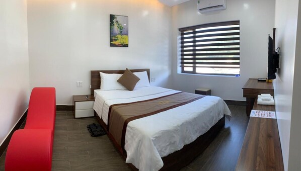 A hotel room with a bed, a red bench, a desk, a window with blinds, and a painting on the wall. - Win Win Hotel (Hai Phong)