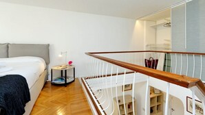 Ein Schlafzimmer mit Bett, Nachttisch, Lampe und Blick auf eine Treppe.