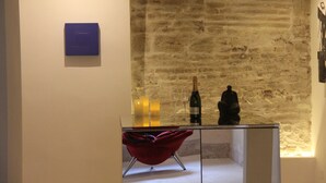 Ein Zimmer mit Backsteinwand, einem roten Sessel, einem kleinen Tisch mit Flasche und Gläsern sowie einer blauen Plakette an der Wand.