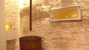 Ein rustikales Badezimmer mit Steinwand, Holzfass und einem gelben Kunstwerk im Bilderrahmen.