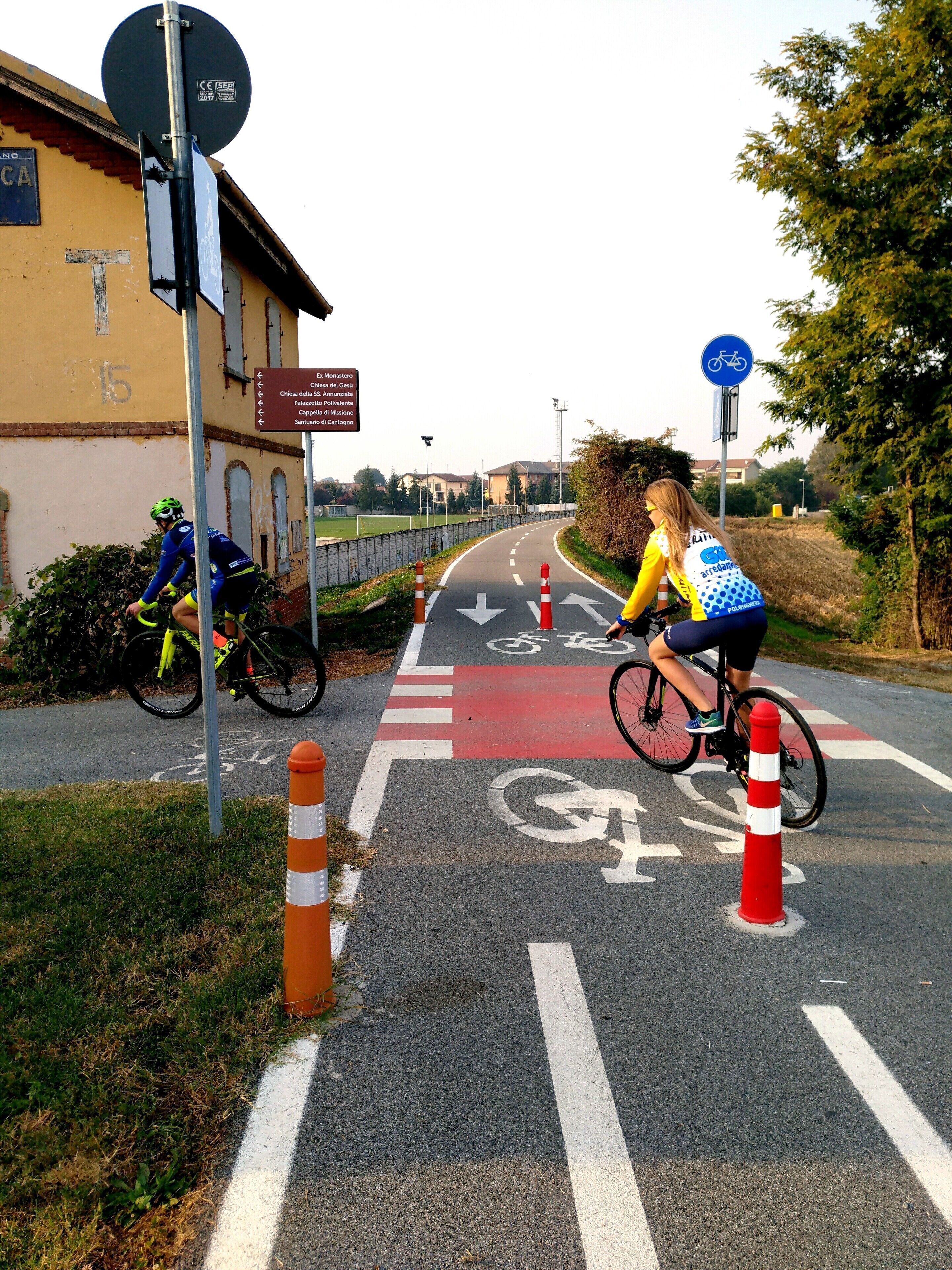 Een fietser op een aangegeven fietspad, met pijlen die de richting aangeven en een bord met vermelding van nabijgelegen plaatsen.