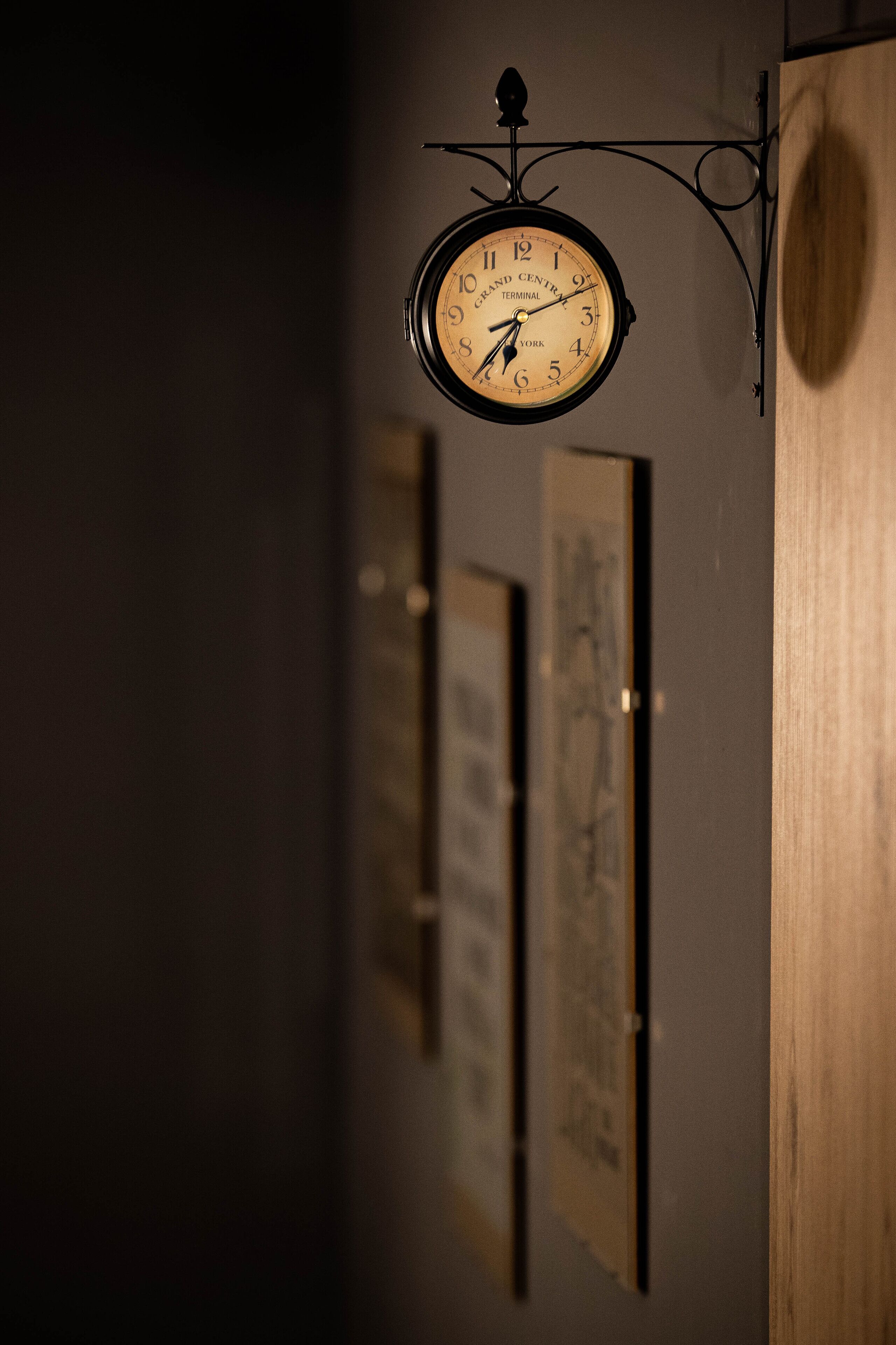 Reloj de pared con diseño clásico, colgado de un soporte metálico curvo.
