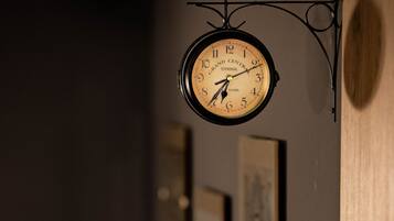 Reloj de pared con diseño clásico, colgado de un soporte metálico curvo.