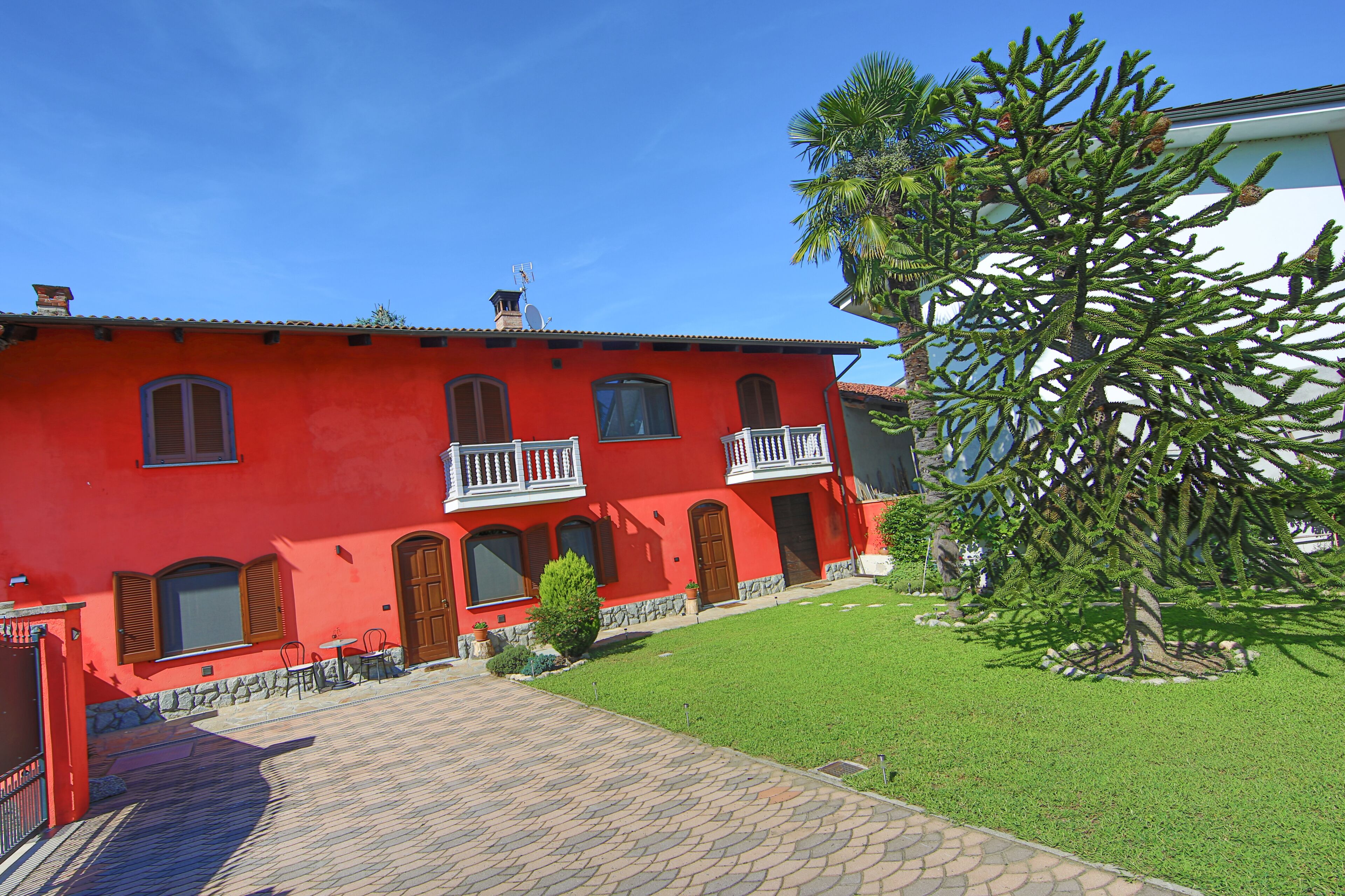 Un edificio rojo con balcón, un pequeño césped y un árbol.