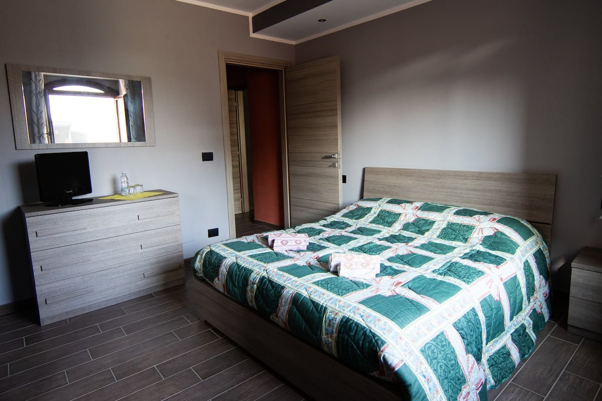 A bedroom with a bed, dresser, TV, and a mirror.
