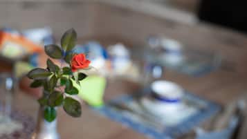 A close-up of a red rose in a vase on a table with blurred background items.