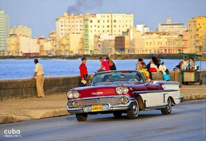 A vintage car driving along a waterfront road with people standing by the edge of the road. - Calle Habana Colonial Home 2 - Old Havana (Havana)