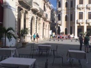 Un área de café al aire libre con mesas y sillas, rodeada de edificios históricos con arquitectura clásica.
