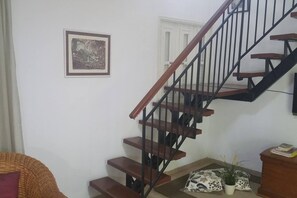 Staircase leads to an upper floor, flanked by a framed picture and a wicker chair.