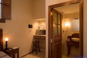 Compact room with a kitchenette, featuring a microwave, countertop, and cabinet, as well as a bathroom with a sink and mirror.