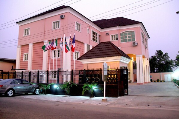 A pink building with multiple flags, a gated entrance, and a parked car. - Queensgate Continental Hotel and Suites (Port Harcourt)
