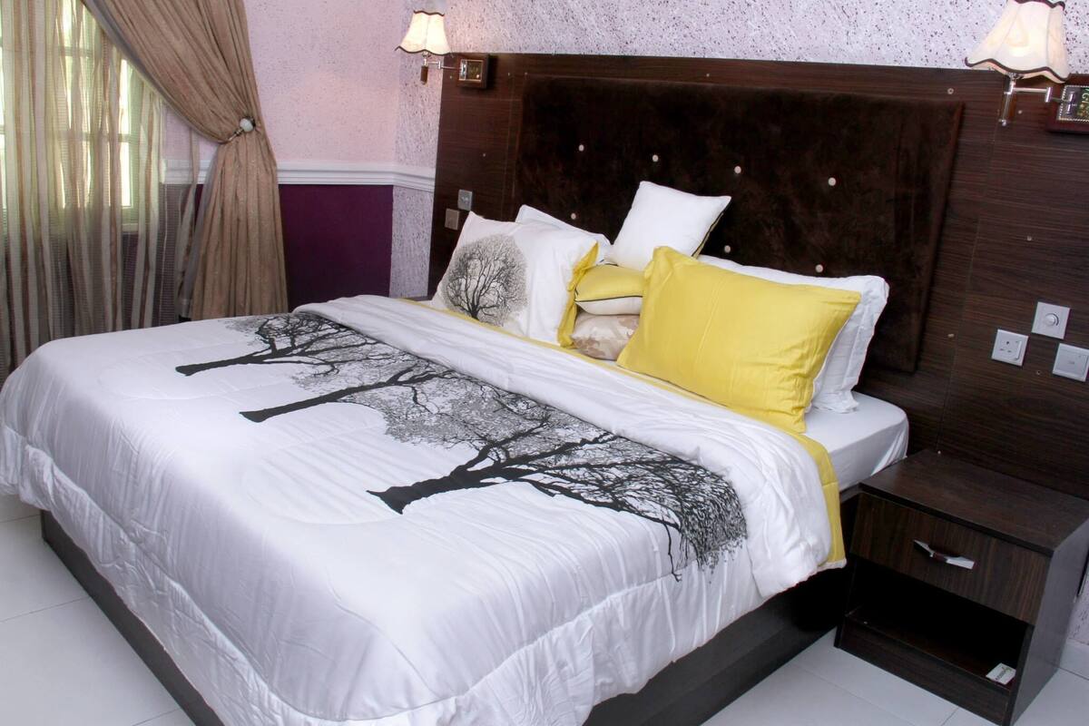 A hotel room with a large bed, a wooden headboard, a nightstand, and a lamp.