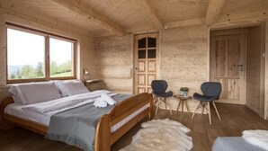 Une chambre dans une cabane en bois, avec un lit, deux chaises, une petite table et une porte.