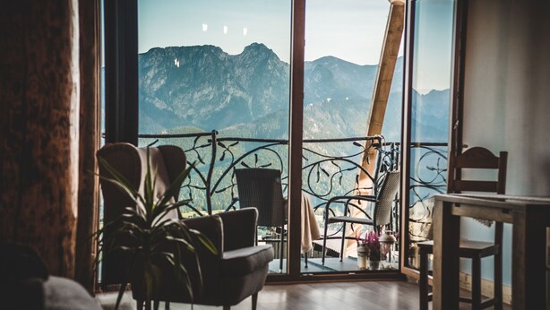 Une pièce dotée d’une grande fenêtre donnant sur les montagnes, d’une chaise, d’une table et d’une plante en pot.