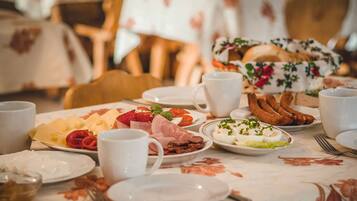 Une table mise pour le petit-déjeuner, avec des assiettes remplies de nourriture, notamment du fromage, de la charcuterie et des œufs, ainsi que plusieurs tasses blanches.