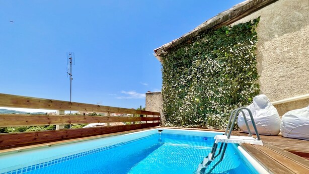 A swimming pool with a wooden deck and a stone wall covered in foliage.