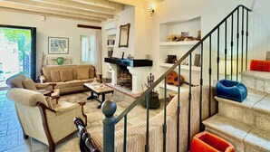 A spacious living room with a high wooden ceiling, a fireplace, and a staircase with metal railings.
