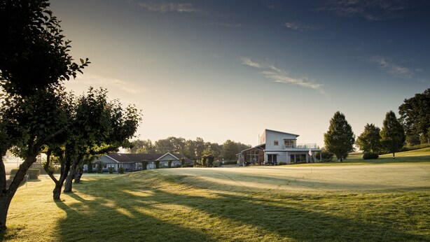 A grassy field with a building that has a modern design, surrounded by trees. - Södersens Golf Lodge (Billesholm)