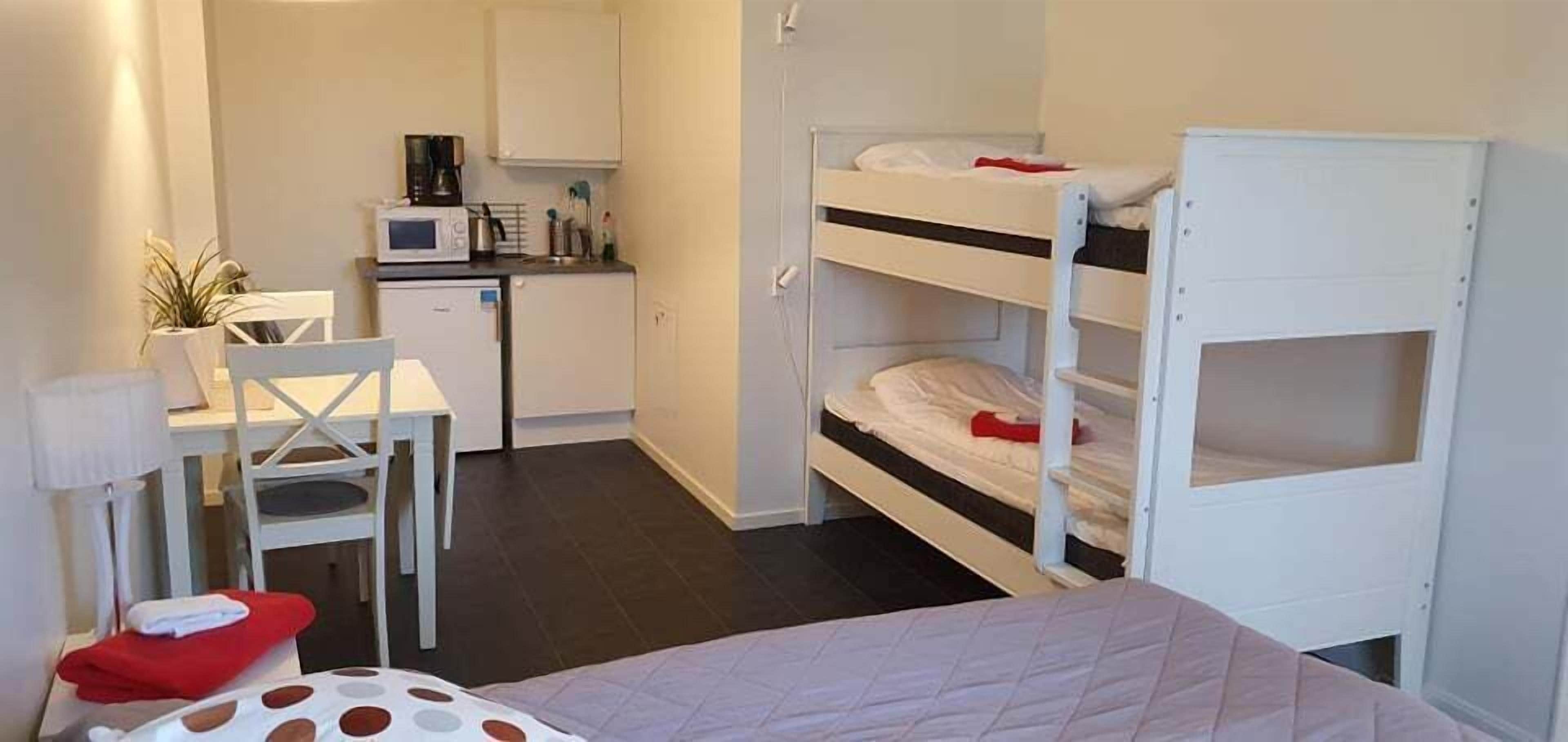 A compact room with bunk beds, a kitchenette, a small dining table, and a chair.