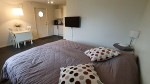 A hotel room with a large bed, a desk with a chair, a flat-screen TV mounted on the wall, and a small kitchenette area. - Södersens Golf Lodge (Billesholm)