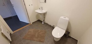 A small bathroom with a toilet, sink, and a rug on the floor. - Södersens Golf Lodge (Billesholm)