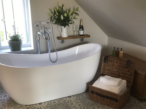 A large freestanding bathtub in a bathroom with a potted plant, a wine bottle, and toiletries on a shelf. - The Old Dower House (Whitchurch)