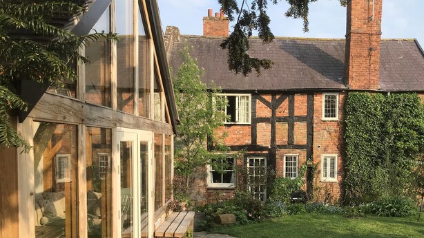 Une maison traditionnelle à colombages, dotée d’une véranda en verre, d’un chemin en pierre et d’une pelouse bien entretenue.