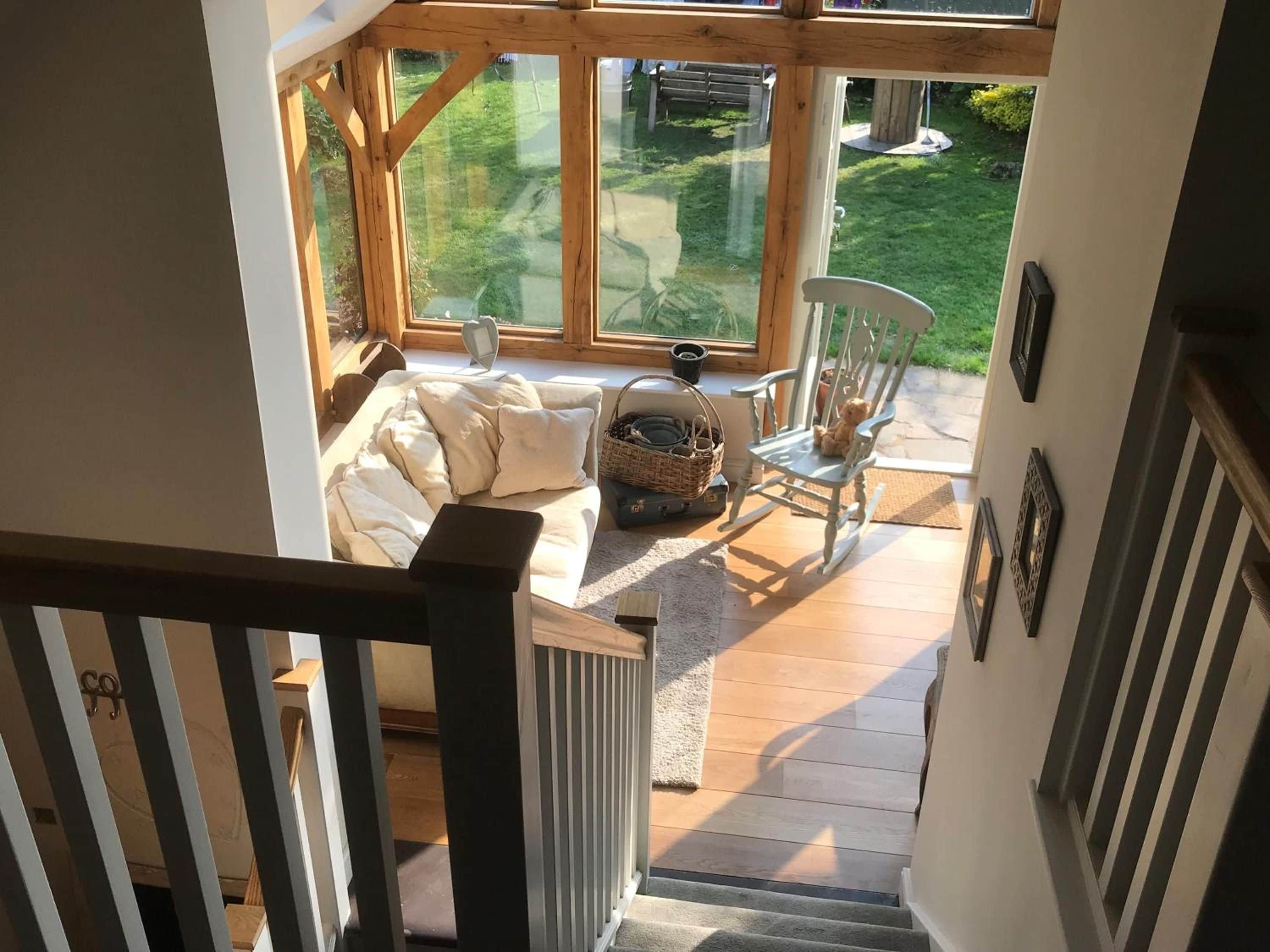 A wooden staircase leading to a room with a sofa, a chair, and a window overlooking a garden.