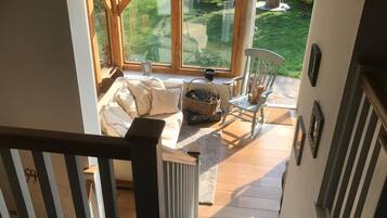 A wooden staircase leading to a room with a sofa, a chair, and a window overlooking a garden.