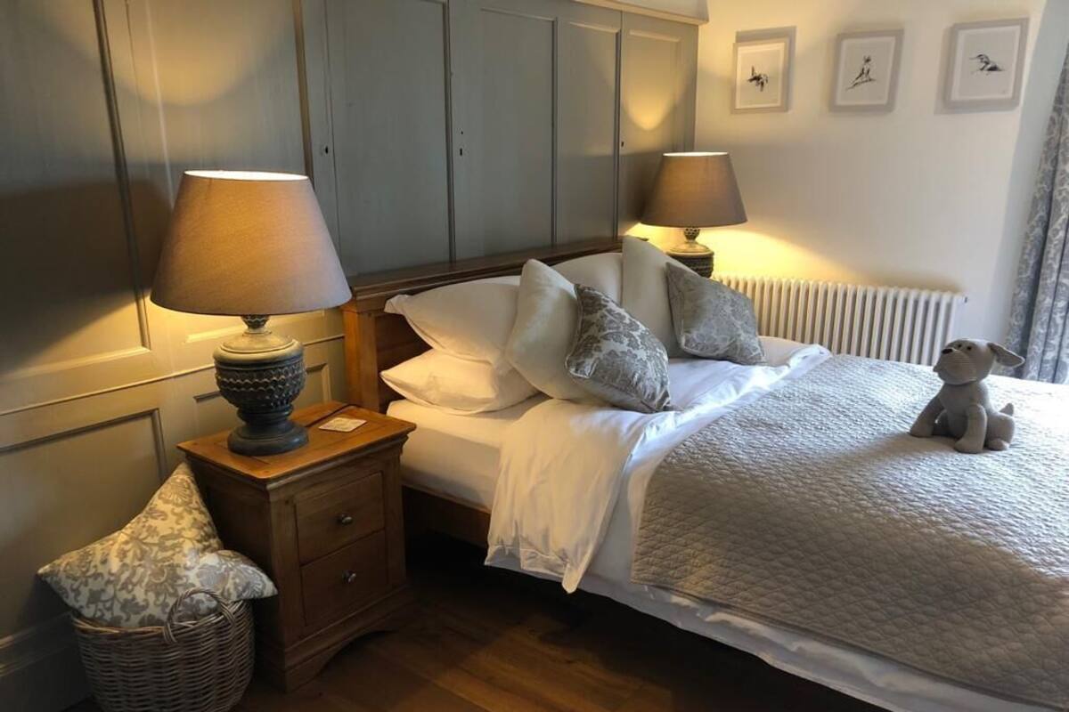 A neatly arranged bedroom with a bed, bedside lamps, a nightstand, a wicker basket, and a teddy bear.