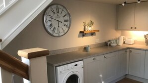 Une cuisine moderne équipée d’un lave-linge encastré, d’une horloge et d’une étagère ornée d’objets décoratifs.