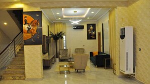 A spacious hotel lobby with a marble floor, a staircase, a large painting, a modern chandelier, and a large air conditioning unit. - Brighams Suites (Lagos)